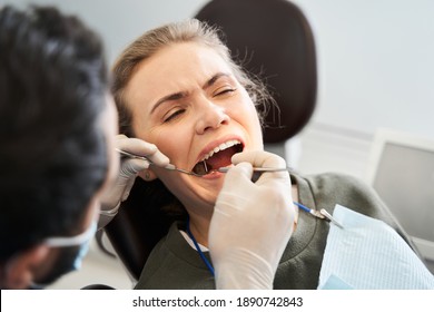 Proper work. Young beautiful blond-haired lady having her teeth examined by serious doctor wearing protective gloves. Examination and inspection at the dental clinic