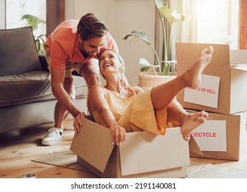 Property, buying and fun couple moving into a new house together, being playful, bonding and unpacking. Happy young husband and wife playing with boxes, laughing and having fun being silly at home