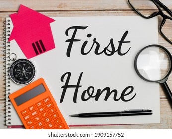 Property Concept. Top View Text First Home Written On Notebook With Pen,calculator,magnifying Glass,cupboard House,compass And Eye Glasses On Wooden Table.