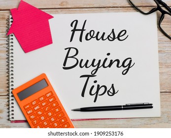 Property Concept. Top View Text House Buying Tips Written On Notebook With Pen,calculator,magnifying Glass,cupboard House,compass And Eye Glasses On Wooden Table.