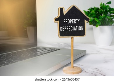 Property Depreciation Text On Wooden House Model With Notebook And Potted Plant White Table. Real Estate Property Concept.