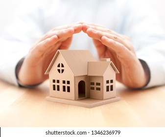 Property insurance. House miniature covered by hands. 