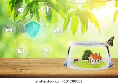 Property Insurance, Toy House In Glass Dome On Wooden Floor. Shield Protection Insurance Icon On Virtual Screen, Against Blurred Natural On Backdrop.