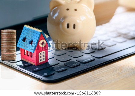 Property investment, homeloan and mortgage concept. Wooden house model, stack of coins and  ceramic piggy bank on tablet keyboard.