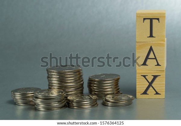 property tax and cars,\
concept, stack of coins on a gray background and the inscription\
tax on wooden cubes