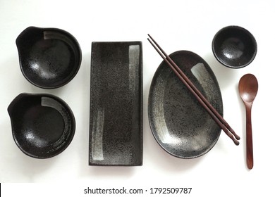 Props. Tableware. Set of black ceramic empty plates, Handmade pottery, spoon and chopsticks wood. Top view on white background
