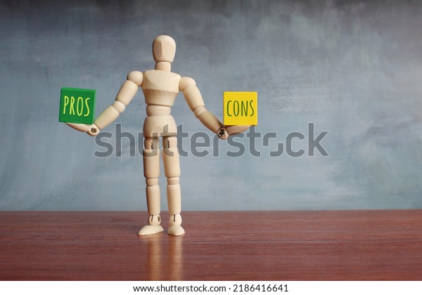 Pros\
and Cons balance concept. Wooden human figure balancing wooden\
cubes with text PROS and CONS. Copy space for\
text
