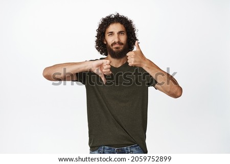 Pros and cons. Young handsome middle-easter man showing thumbs up and thumbs down, like or dislike, standing over white background