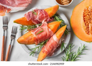 Prosciutto Ham With Melon Cantaloupe Slices, Honey And Rosemary In A Plate With Forks On White Background. Italian Appetizer. Top View. Healthy Food