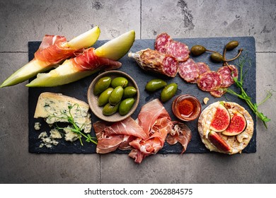 Prosciutto Ham, Slices Of Melon, Brie And Gorgonzola Cheese, Honey And Olives On Gray Background, Top View