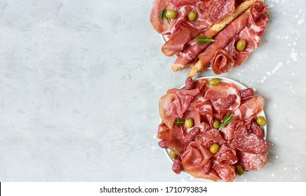 Prosciutto Jamon Parma Ham Salami Smoked Sausage And Olives With Grissini Breadsticks On A White Plate. Serving Appetizers For An Aperitif, Lunch, Dinner And Holiday. Catering, Food Delivery