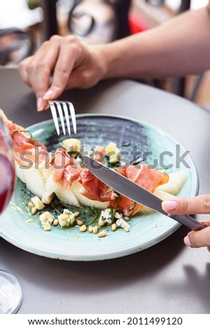 Prosciutto and melon salad at restaurant. Young woman eating Italian salad outside. Italian cuisine concept.