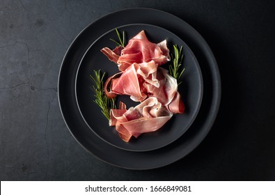 Prosciutto and rosemary on a black plate. Top view, copy space.