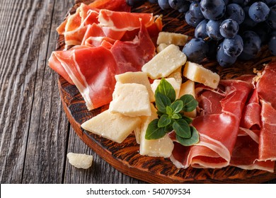 Prosciutto, wine, grape, parmesan on wooden table, selective focus.