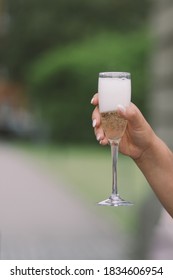 A Prosecco Glass In A Woman's Hand Outdoors With Green Background