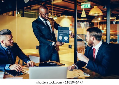 Prosperous Executive Manager Holding Graphic And Charts Communicating With Crew Of Colleagues In Meeting Table, Diversity Group Of Male Entrepreneurs Analysing Sponsorship Idea Using Illustration Data