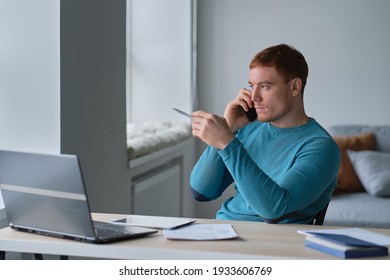 Prosperous Young Male Freelancer Making Telephone Call While Working Remotely On Laptop Computer In Coworking Office , Handsome Smiling Hipster Guy Enjoying Mobile Phone