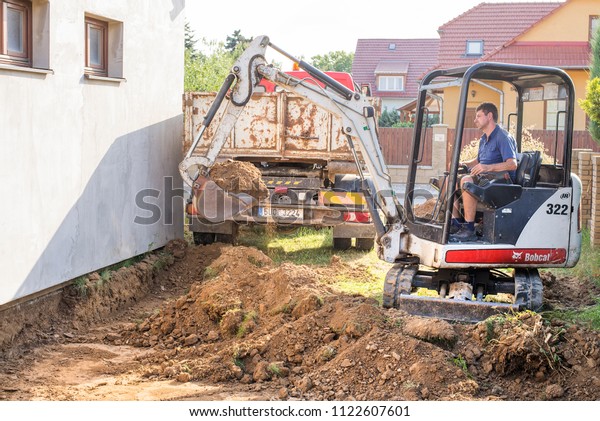 Prostejov Czech Rep 19.6.2018 Mini\
excavator on construction site. Excavator regulates the terrain\
around the house. Digger digging soil and loading it on a\
lorry.