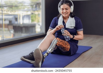 Prosthetic leg amputee woman sit relaxing in gym. Asian female with foot prosthesis enjoy listen to music in fitness. Artificial limb mechanical help accident survivor, body injury people to mobility. - Powered by Shutterstock