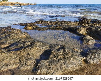 Protaras. Famagusta area. Cyprus. The coast of the Mediterranean Sea, long frozen lava, in the recesses of which there is sea water against a blue sky with clouds.