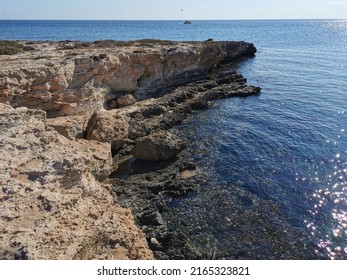 Protaras. Famagusta area. Cyprus. A rocky shore of long-hardened lava, a cliff, the Mediterranean Sea with a boat, against the background of a blue cloudless sky.