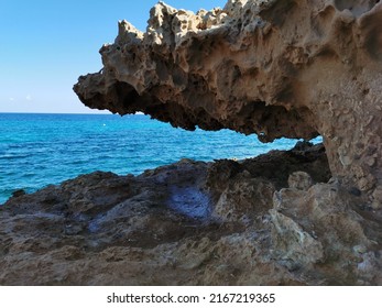 Protaras. Famagusta area. Cyprus. A stone, a rock, a hanging piece of long-frozen lava, below dried salt, similar to ice, against the background of the sea and a blue cloudless sky.