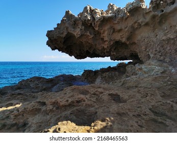 Protaras. Famagusta area. Cyprus. A stone, a rock, a hanging piece of long-frozen lava, below dried salt, similar to ice, against the background of the sea and a blue cloudless sky.
