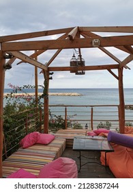 Protaras. Famagusta. Cyprus. Cafe Next To The Beach, No People. Tents With Soft, Low Mattresses, Scattered Multi-colored Pillows, A Decorative Bird Cage And A Glass Square Table Against A Cloudy Sky.