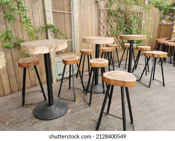 Protaras. Famagusta Region. Cyprus. Cafe Next To The Beach, No People. Tables And Bar Stools Made From Sawn Wood Against A Wooden Wall Covered With Climbing Plants.