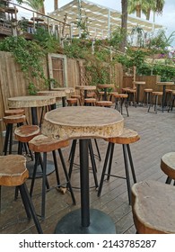 Protaras.Cyprus.10.21.2021. Famagusta Region.Cafe Next To The Beach, No People. Tables And Bar Stools Made From Sawn Wood Against A Wooden Wall Covered With Climbing Plants.