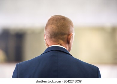 Protect Guard Or Secret Service Agent Listening To His Earpiece On Public Meeting. Back View