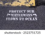 Protect Our Waterways - Flows To Ocean message stencilled onto a road