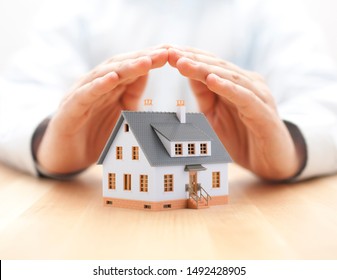 Protect your house concept. Small toy house covered by hands