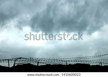 Protected area surrounded with wall and barber wire. Barbed wire used to prevent illegal entry. Barbed wire with dramatic dark clouds on the background.