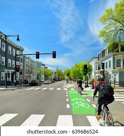 Protected Bike Lane Between Parking Lane And Sidewalk On City Street. Bikers Commuting On Nice Spring Day.