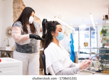 Protected young woman with gloves and mask at the hairdresser consulting current news on her mobile phone while her hair is fixed - Powered by Shutterstock