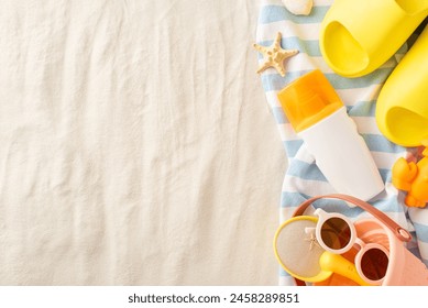 Protecting little ones at the beach. Top view of SPF lotion bottle surrounded by sand play essentials: bucket, shovel, sunglasses, slippers, towel and more. Sandy beach background for your message - Powered by Shutterstock