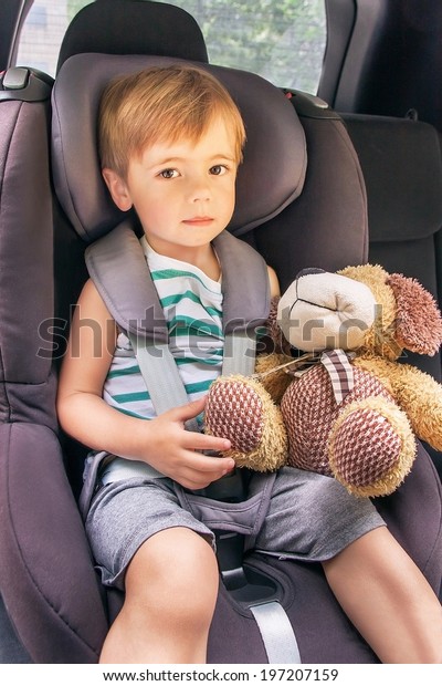 Protection in the car. Caucasian child is\
sitting and fastening with security belt in safety car seat\
(chair).Toddler boy is playing with toy (dog) in the car.  Vehicle\
and transportation\
concept.
