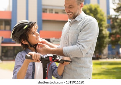 Protection Concept. Daddy teaching his brave son to ride e-scooter, putting safety helmet on him, selective focus - Powered by Shutterstock