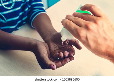 Protection From Covid 19. Sanitizer For Hands. A European Pours Disinfection Gel On The Hands Of A Black Girl At Home. Caring For People During The Coronavirus Pandemic.