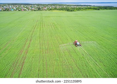 Protection of green seedlings from diseases, pests and weeds. Self-propelled sprayer working in the field. In the distance the village on the shore of the pond. Shot from a drone. - Shutterstock ID 2251135895