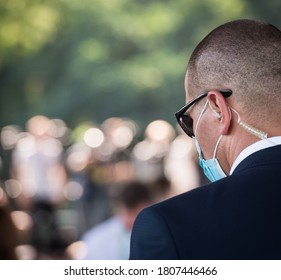 Protection And Guard Service. Bodyguard Man With Earphone And Black Eyeglasses And Business Suit Wearing A Mask During The Covid Outbreak, During A Public Visit Of A Dignitary.