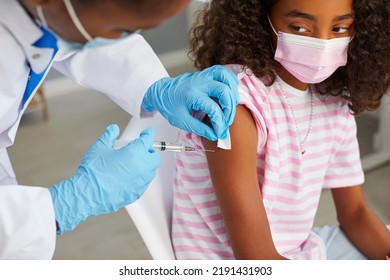 Protection And Immunization Of Population With Covid-19 Vaccine. Nurse Gives Covid 19 Vaccine To Dark-skinned Teenage Girl Who Is Sitting In Medical Mask. Doctor Disinfects Injection Site. Close Up.