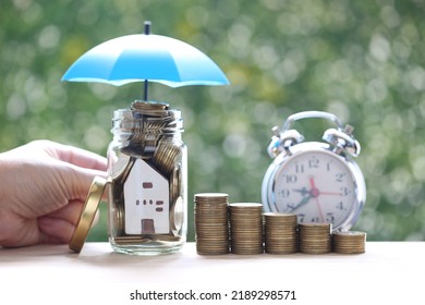 Protection, Model house and gold coin money in the glass bottle under the umbrella on natural green background, Finance insurance and Safe investment concept