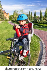 Protection on the bicycle. Baby boy is in the bicycle chair (seat) with a biking helmet on  head and bottle of water in hands during bicycle ride. Child has trip in the summer day. Travel concept. 