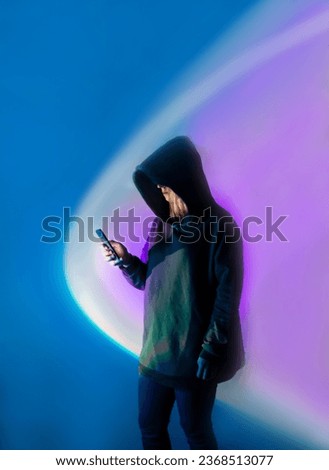Protection of personal data on a mobile device. Anonymous human with mobile phone against bright multicolored neon light.
