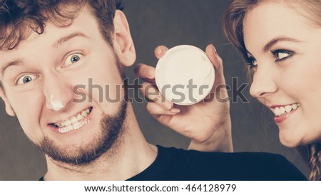 Protection and skincare. Stubborn girlfriend trying to apply cream on her boyfriend face. Man in uncomfortable situation with overprotective woman.