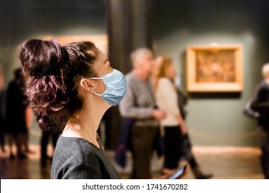 Protection from the virus. A tourist visits the sights of the Museum in a medical mask. People and pictures in the background. The concept of a viral pandemic and maintaining distance