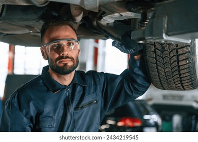 In protective eyewear, under vehicle. Car repairman is in the garage with automobile. - Powered by Shutterstock