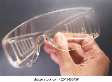 Protective Glasses In Hand, Healthcare And Safety Concept. Safety Glasses On Black Background. Personal Protective Equipment. Plastic Goggles, Transparent Glasses Safety At Work